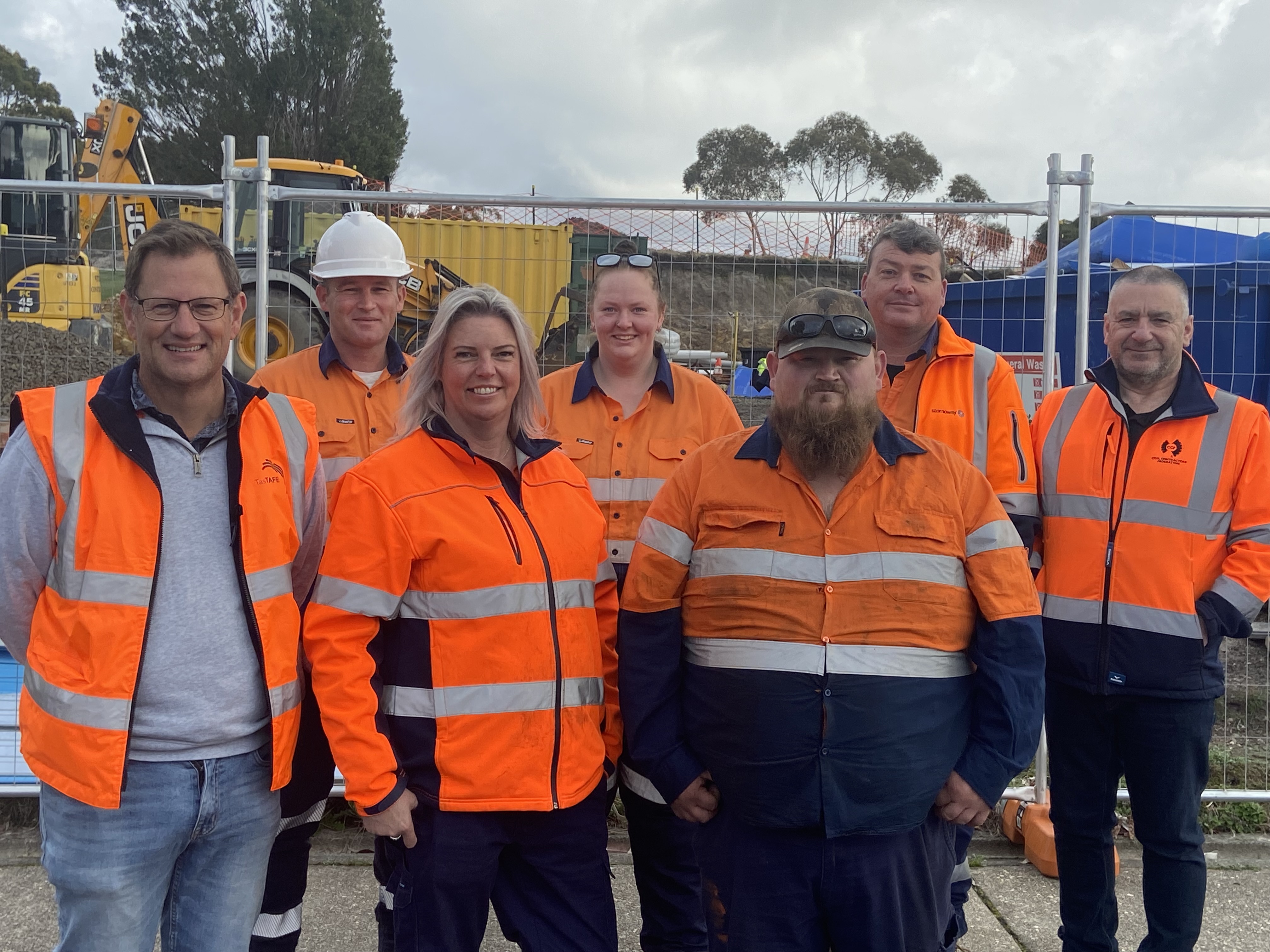 7 people in front of a construction site wearing Hi Vis clothing