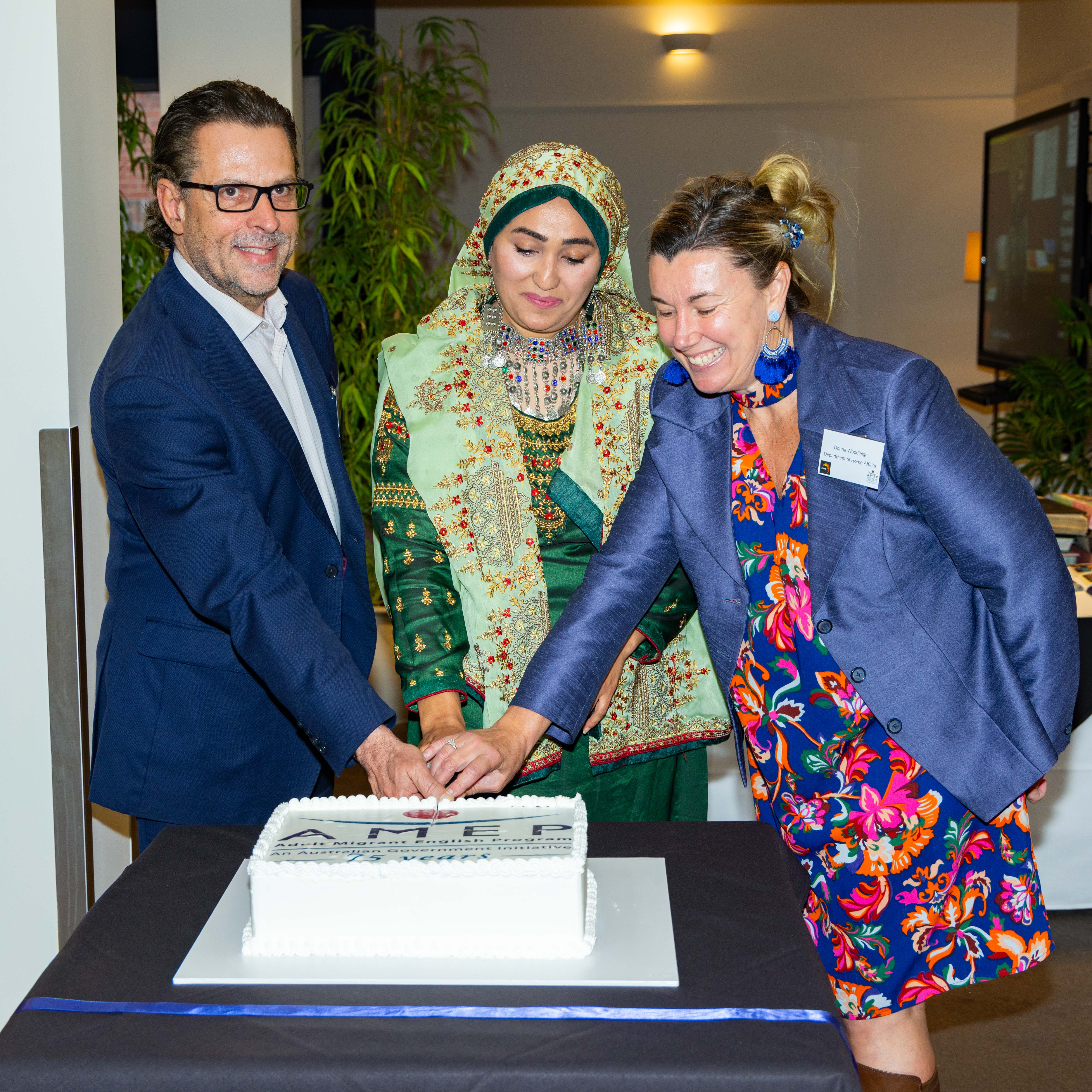 TasTAFE CEO Grant Dreher and 2 woman cut a cake with the AMEP logo on it