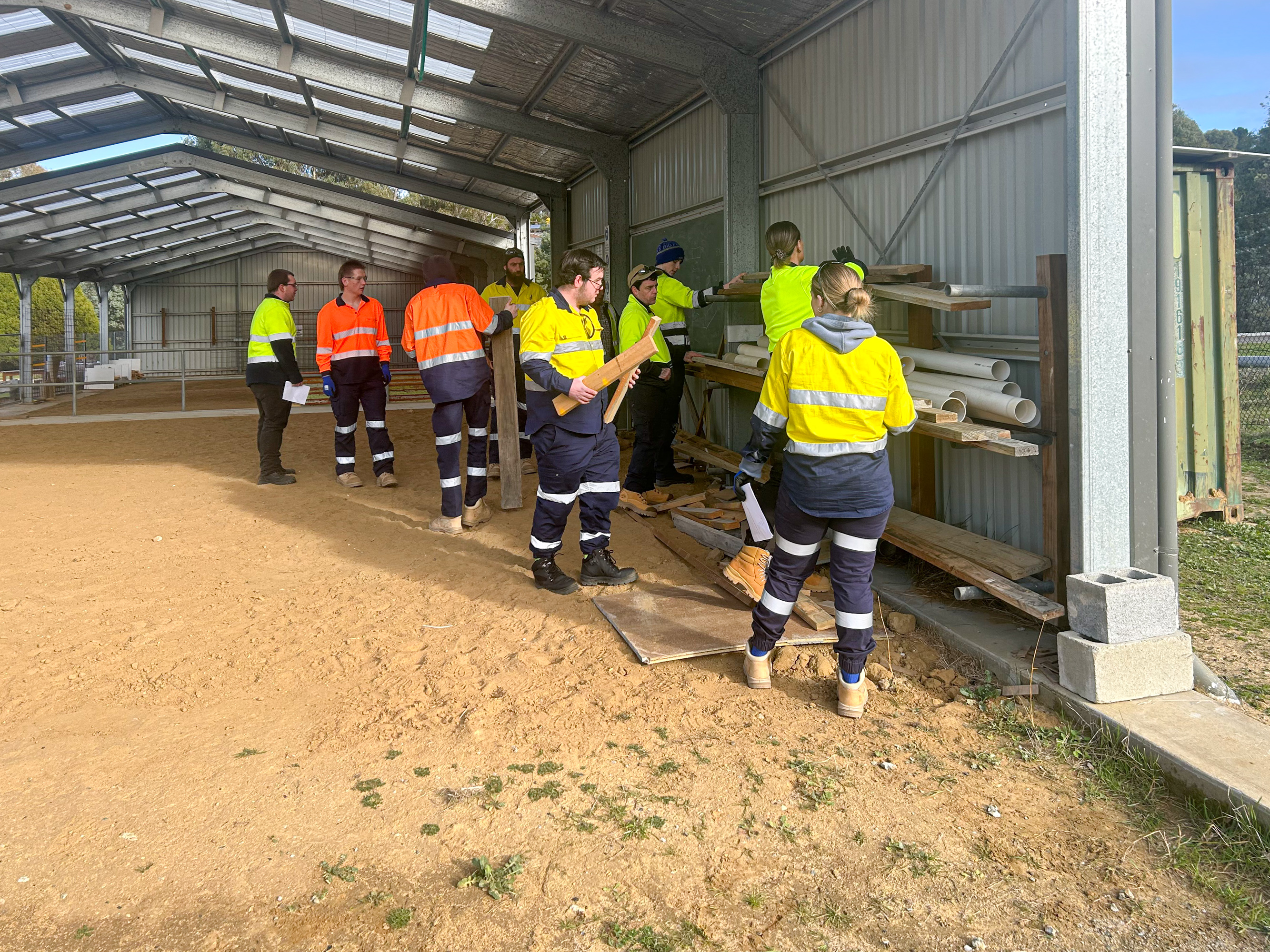 Group of people in Hi Vis in a farm shed with wood and PVC pipes